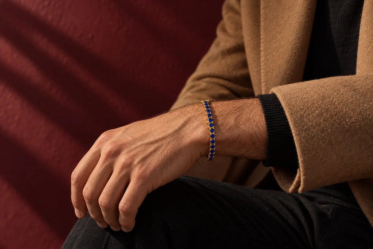 Uomo mediterraneo, camicia bianca di lino con manica arrotolata, polso sinistro con orologio d'acciaio e bracciale tennis sottile accostato, luce dorata di fine pomeriggio, sfondo muro di tufo napoletano sfocato