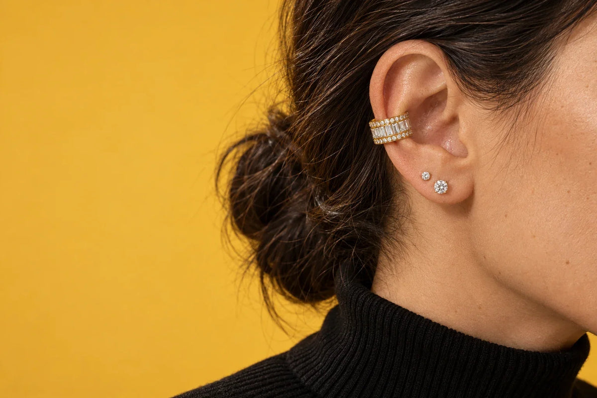 Modella mediterranea, capelli scuri raccolti in uno chignon basso, profilo a tre quarti, ear cuff in argento 925 sulla conca e due punti luce sul lobo, luce invernale da finestra, maglione di lana color avena